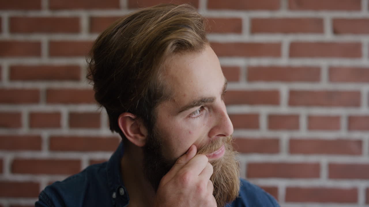retrato de un joven y guapo hipster con barba que mira pensativo un hombre caucásico barbudo sonriendo feliz en cámara lenta