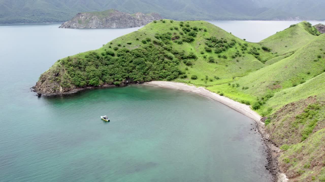 Drone descends into tropical Costa Rica island, with lush hills and turquoise waters below, strip of sand beach hidden and lone boat anchored