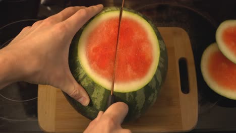 Schneiden-Sie-Die-Ganze-Wassermelone-Mit-Einem-Küchenmesser,-Das-Auf-Einem-Hölzernen-Schneidebrett-Liegt,-In-Zwei-Hälften---High-Winkel-Aufnahme