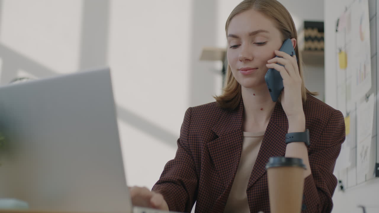 Donna che lavora al portatile e parla al telefono in un ufficio moderno