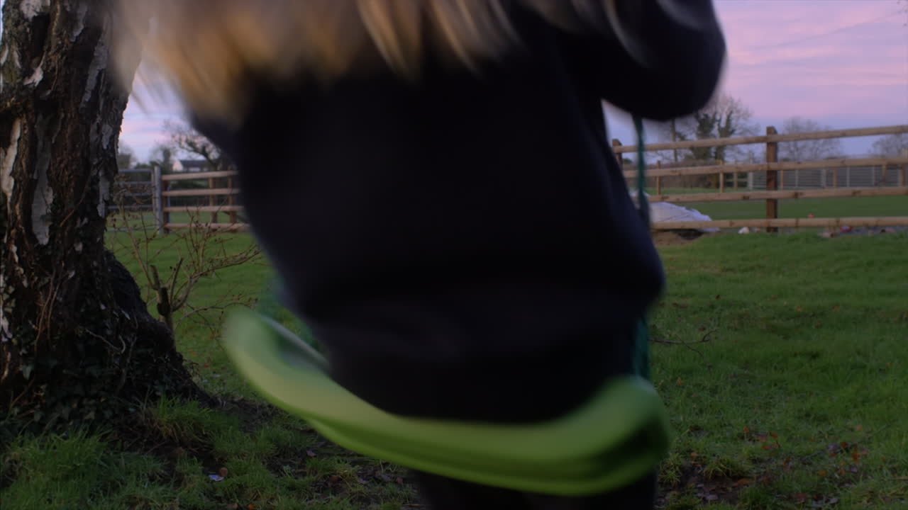 A cute little girl swinging on a swing during sunset in a countryside garden. STATIC SHOT
