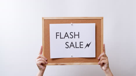 woman's hand shows the paper on board with the word flash sale in white studio background with copy space