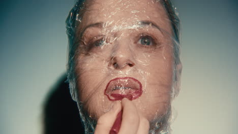 woman with plastic wrap on face applying lipstick