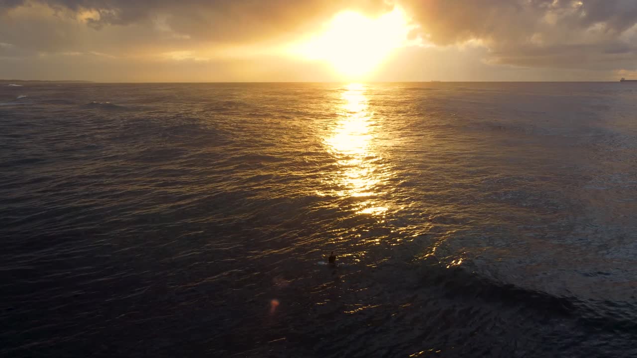 Aerial landscape drone still shot of surfer waiting for waves in morning sun rise reflection on water nature tourism Pacific Ocean Central Coast NSW Australia 4K