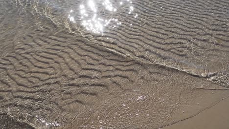 Cámara-Lenta-De-Tranquilas-Olas-Del-Mar-En-Una-Playa-De-Arena-Con-Luz-Reflejada-En-El-Agua