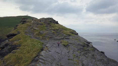 aerial camera follows man as he runs up rugged rocky outcrop in uk