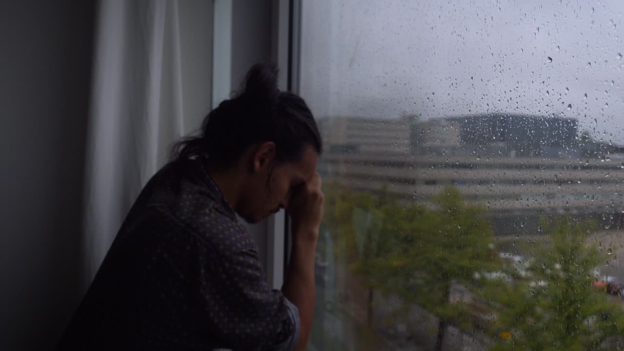 우울한 비오는 날 창문 앞에 팔을 기대고 있는 우울한 남자
