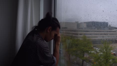 A-depressed-man-leaning-on-his-arm-on-a-gloomy-rainy-day-in-front-of-a-windows