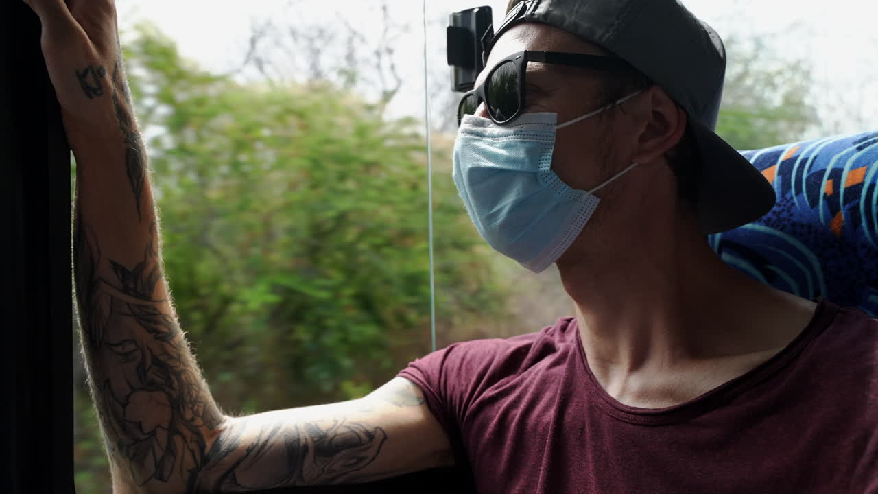 Male Tourist Wearing Face Mask, Sunglasses And Baseball Cap Taking Bus Ride After Arriving On Santa Cruz Island In the Galapagos. Slow Motion