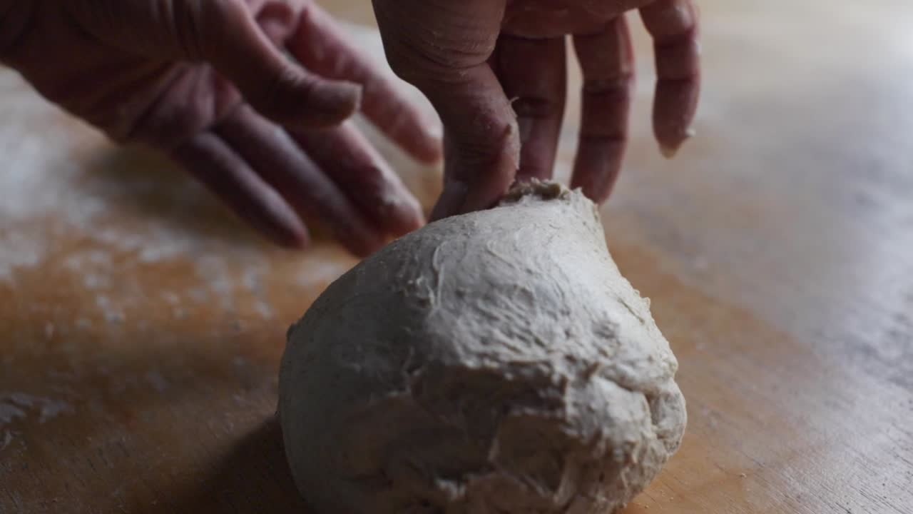 Fresh dough ball being plucked by hands of chef on wooden kitchen tabletop, filmed as closeup slow motion shot