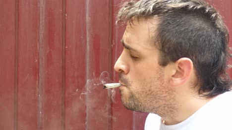 a person lighting a marijuana cigarette, or a cannabis joint in front of a red wall