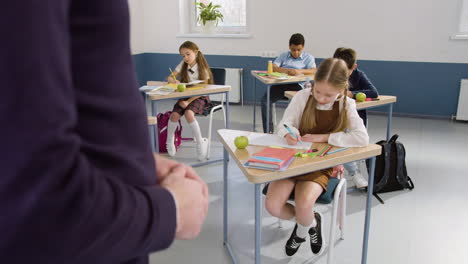 multiethnic group of students sitting at desks in english classroom writing in their notebooks