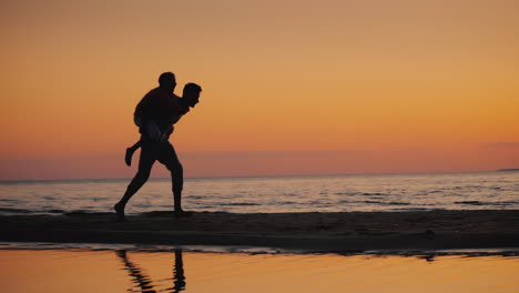 Un-Joven-Juega-Con-Un-Niño-Lo-Lleva-Sobre-Sus-Hombros-En-La-Playa