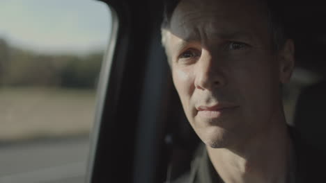 Man-riding-in-a-car-stares-out-the-passenger-side-window-out-at-the-highway-passing-by-and-then-turns-to-stare-ahead