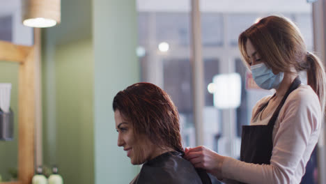 female hairdresser wearing face mask putting cape on female customer at hair salon