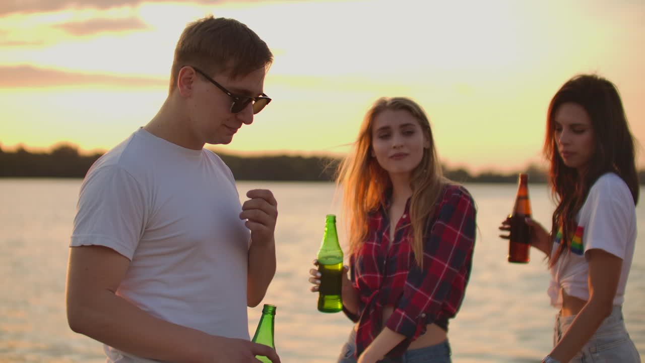 las estudiantes están bailando con cerveza en la fiesta de verano caliente en la playa con su novio en camisetas blancas. disfrutan de esta noche de verano al atardecer.