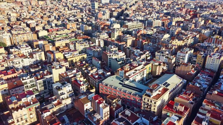 Sorvolando l'iconica griglia urbana del quartiere Eixample di Barcellona, con la cima del Tibidabo tra le dolci colline della catena montuosa di Collserola, che fornisce un drammatico punto di riferimento geografico alla tentacolare capitale catalana