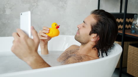 man taking a selfie in a bubble bath with a rubber duck
