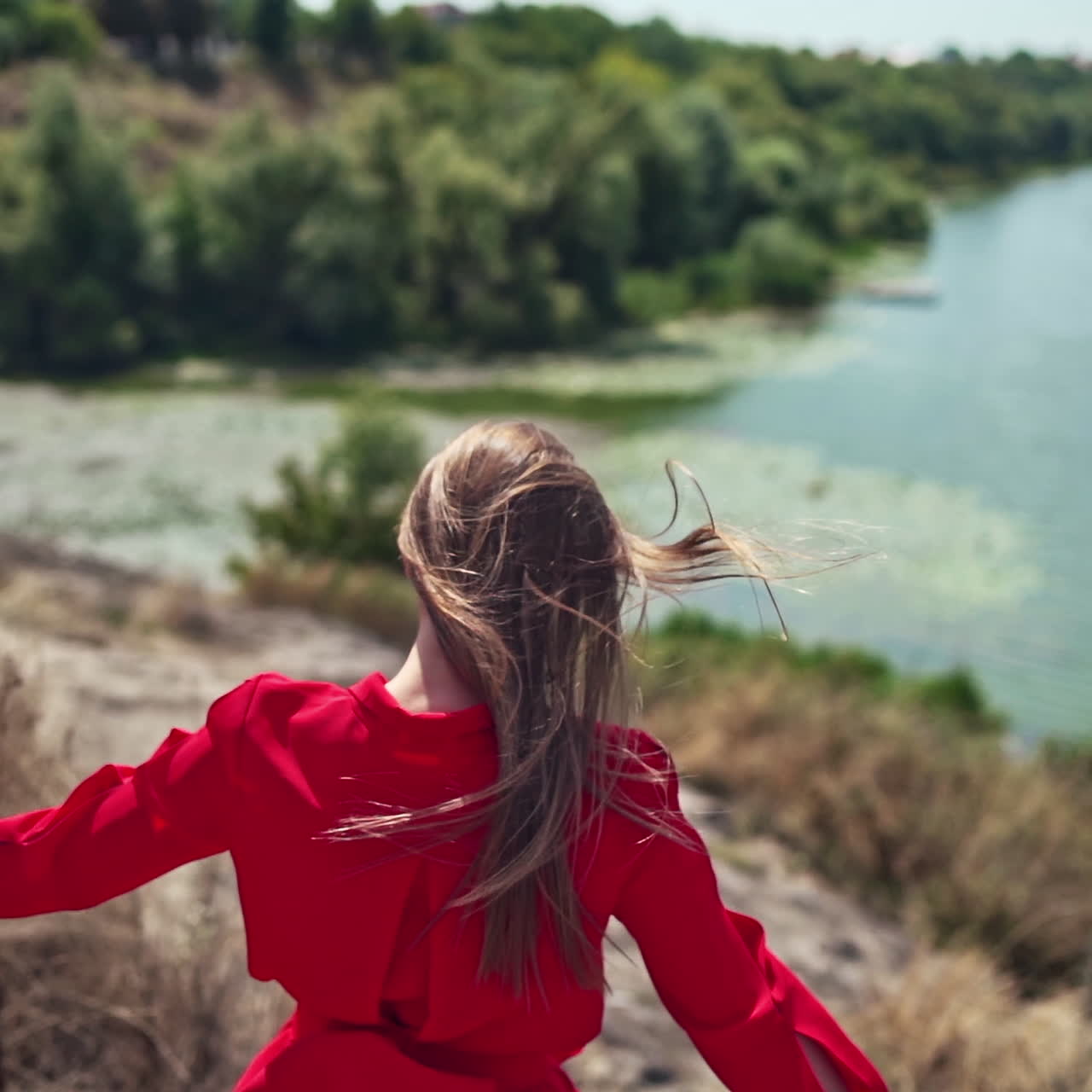 Long haired woman on the natural summer background. Beautiful young lady walking down the hill to the river in a sunny day. Slow motion.