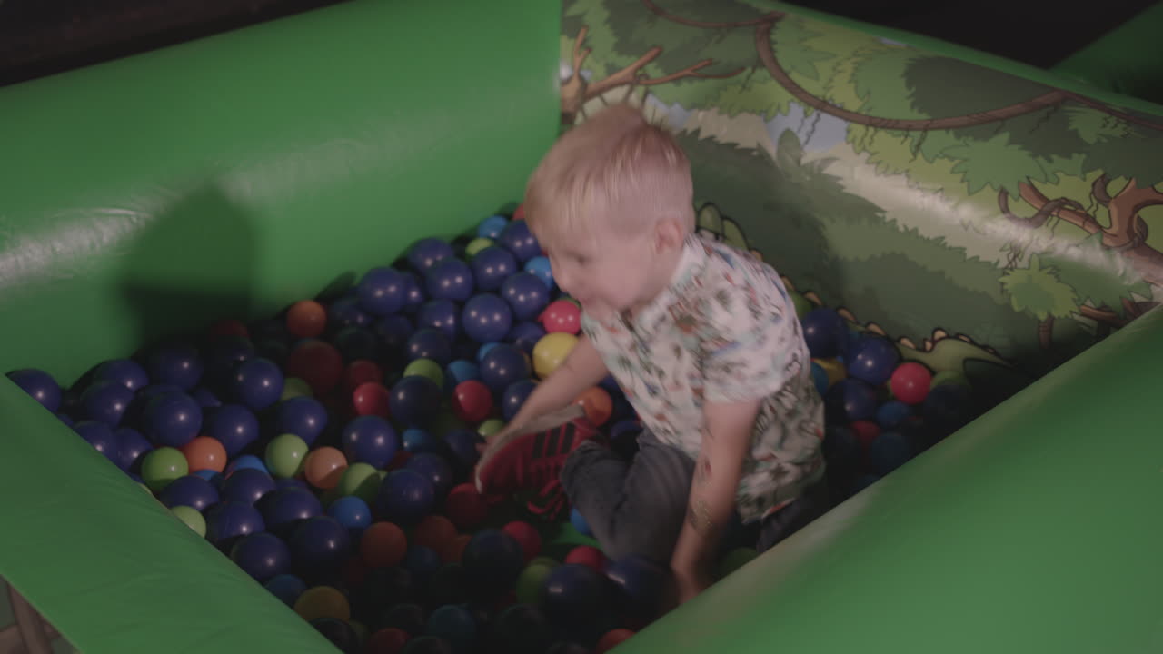 niño jugando en la piscina de bolas, sonriendo y lanzando las bolas