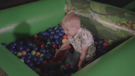 young boy playing in ball pit, smiling and throwing the balls around