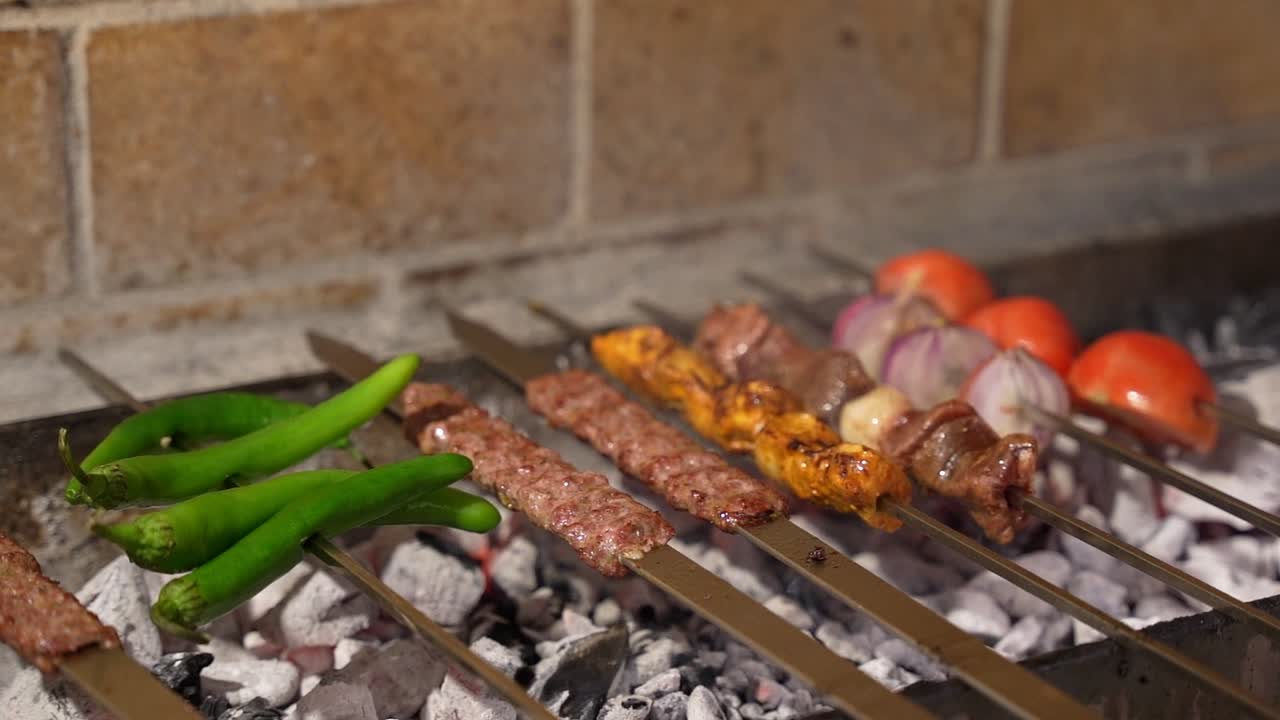 Primo piano di kebab assortiti con carne, pollo, cipolle, pomodori e peperoncini verdi grigliati su spiedini su brace ardente. Una scena di cibo da strada e barbecue sfrigolante, piena di sapore e fumo
