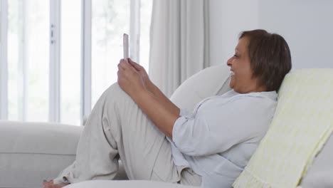 Happy-african-american-senior-woman-sitting-on-couch-making-video-call-using-tablet,-smiling