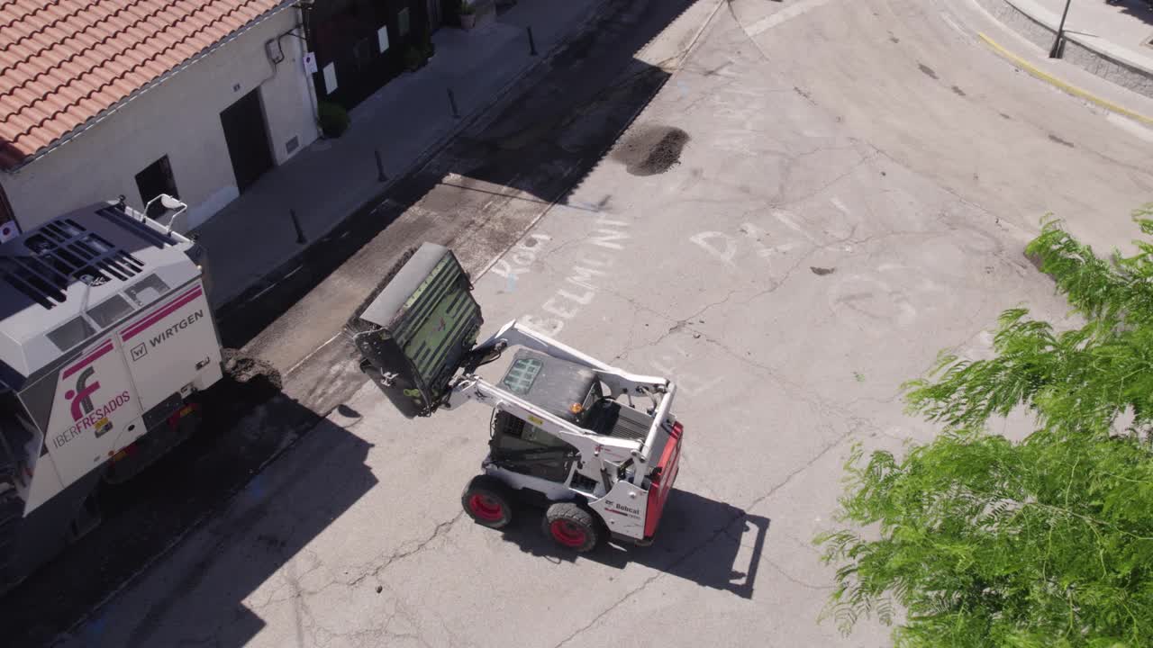 Low angle aerial view of bobcat cleaning after asphalt paver