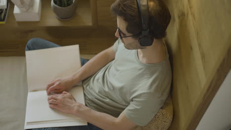 vista superior de un joven caucásico con auriculares tocando un libro