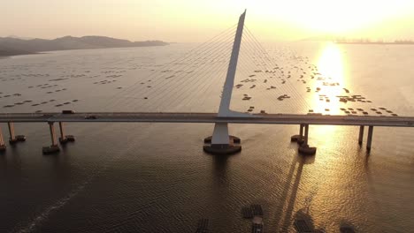 Traffic-on-Hong-Kong-Shenzhen-Bay-Bridge-at-Sunset,-with-Fish-and-Oyster-cultivation-pools,-Aerial-view