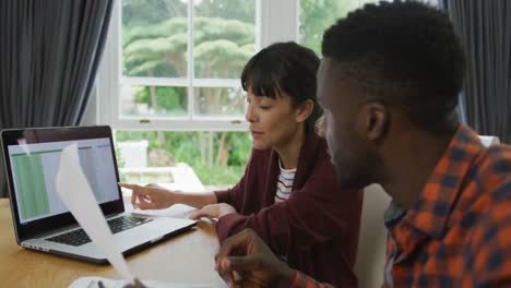 diverse couple sitting at table talking and working with laptop