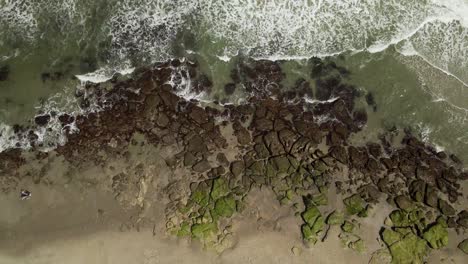 toma hipnótica que sigue las olas rompientes en la costa rocosa de la playa aérea de arriba hacia abajo