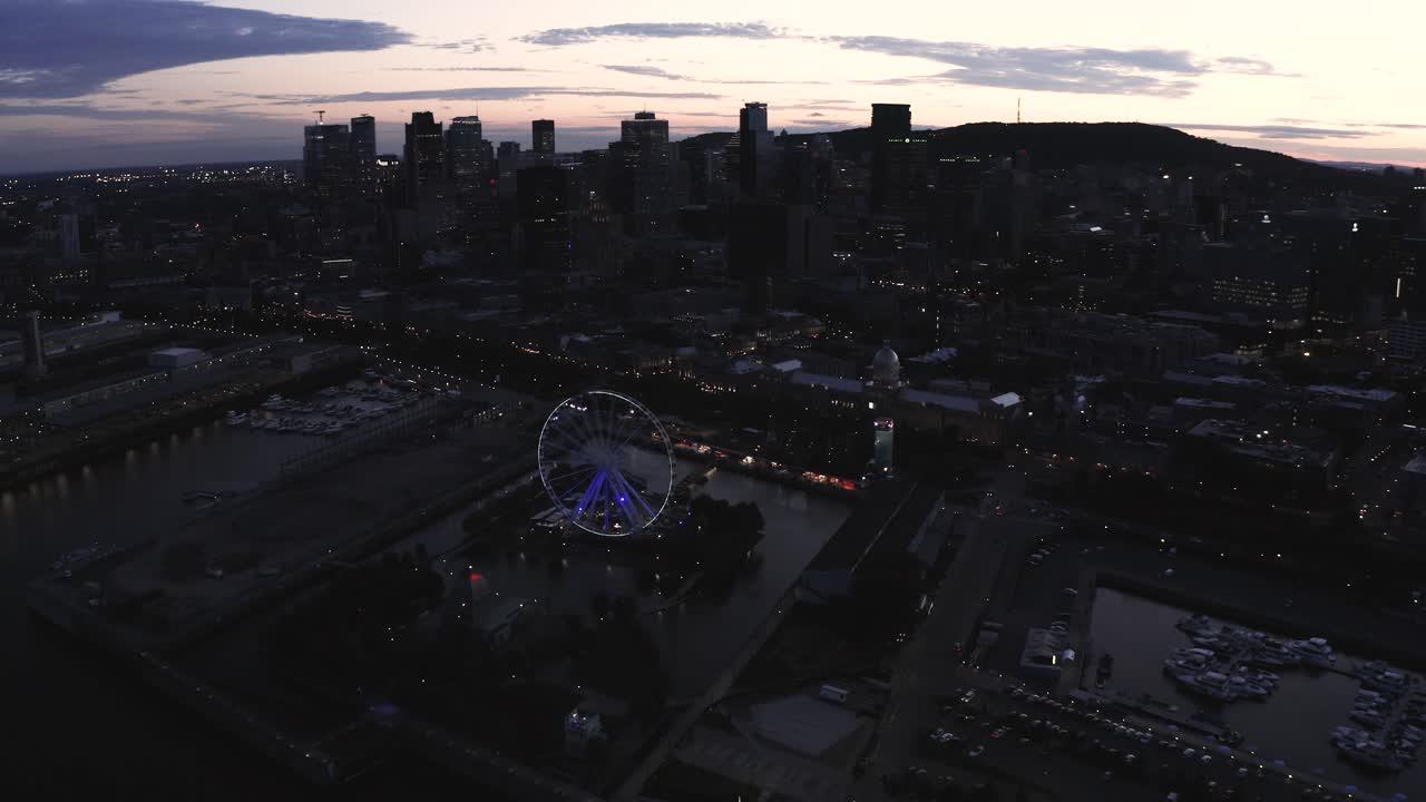 Aerial shot of the Ferris wheel in Montreal's old port as dusk. Sun setting behind the city skyline in the background.