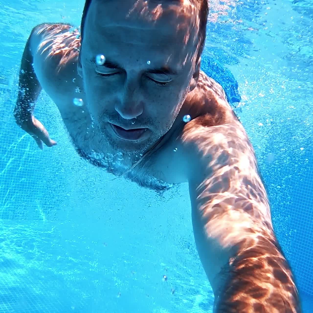 Man jumping into the swimming pool. Healthy man holding underwater camera and jumping into blue water of the pool. Summer vacation.
