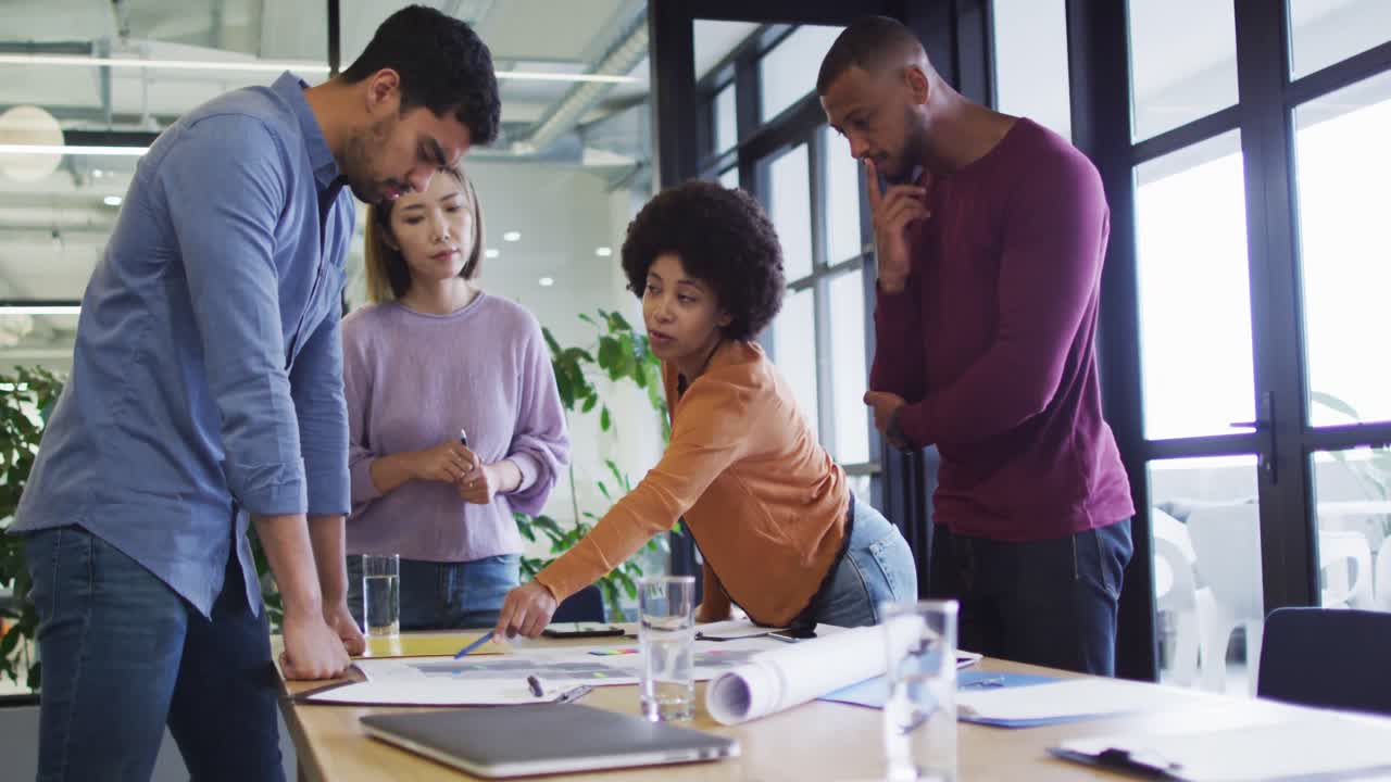Diverse office colleagues wearing face masks discussing over blueprint plan at modern office
