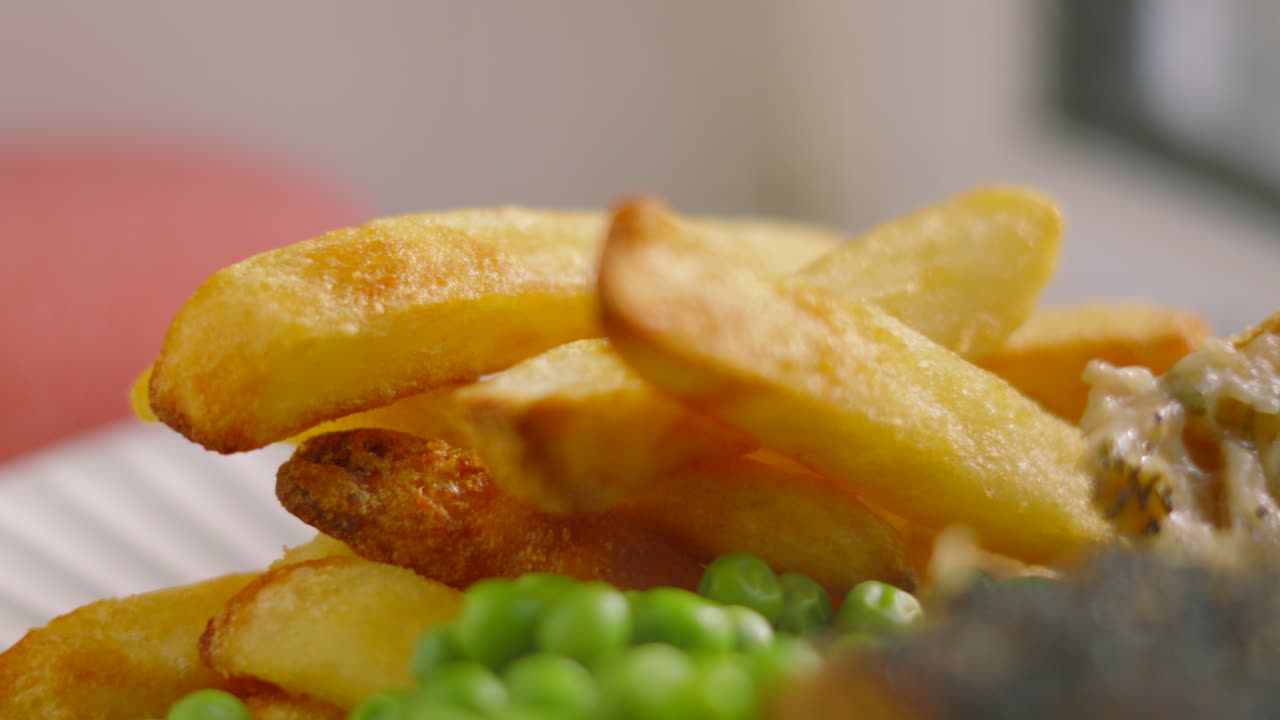 Primo piano statico di patatine fritte spesse appena fatte, su un piatto con piselli sotto