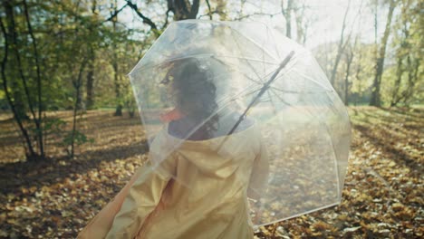 kaukasische frau mit durchsichtigem regenschirm geht im herbstpark spazieren.