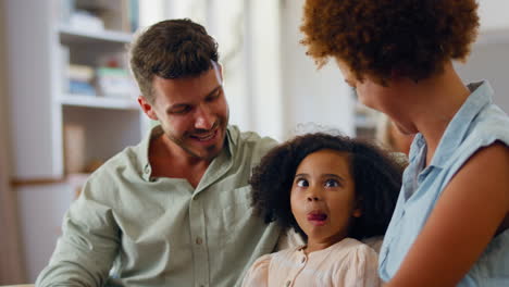 hija sentada con los padres en el sofá en casa haciendo caras graciosas