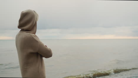 a woman in a warm knitted sweater looks at the sea where the storm begins