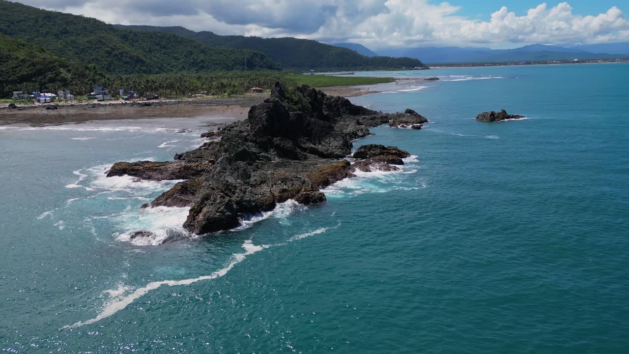 A wide-angle drone shot captures the small rocky mountains along the shore, stretching out as the ocean waves gently lap at the base of the rocks.