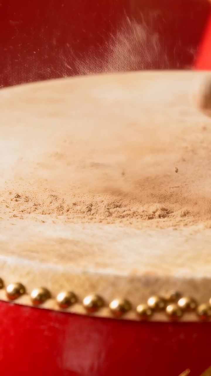 Vertical video: Striking drumstick hitting beige drumhead in closeup, lifting dust plume with studs