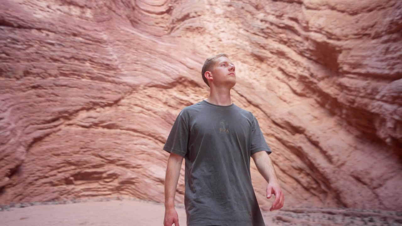 Un uomo ammira con stupore le formazioni rocciose rosse in un canyon desertico nel tardo pomeriggio, guardando verso l'alto - piano medio.