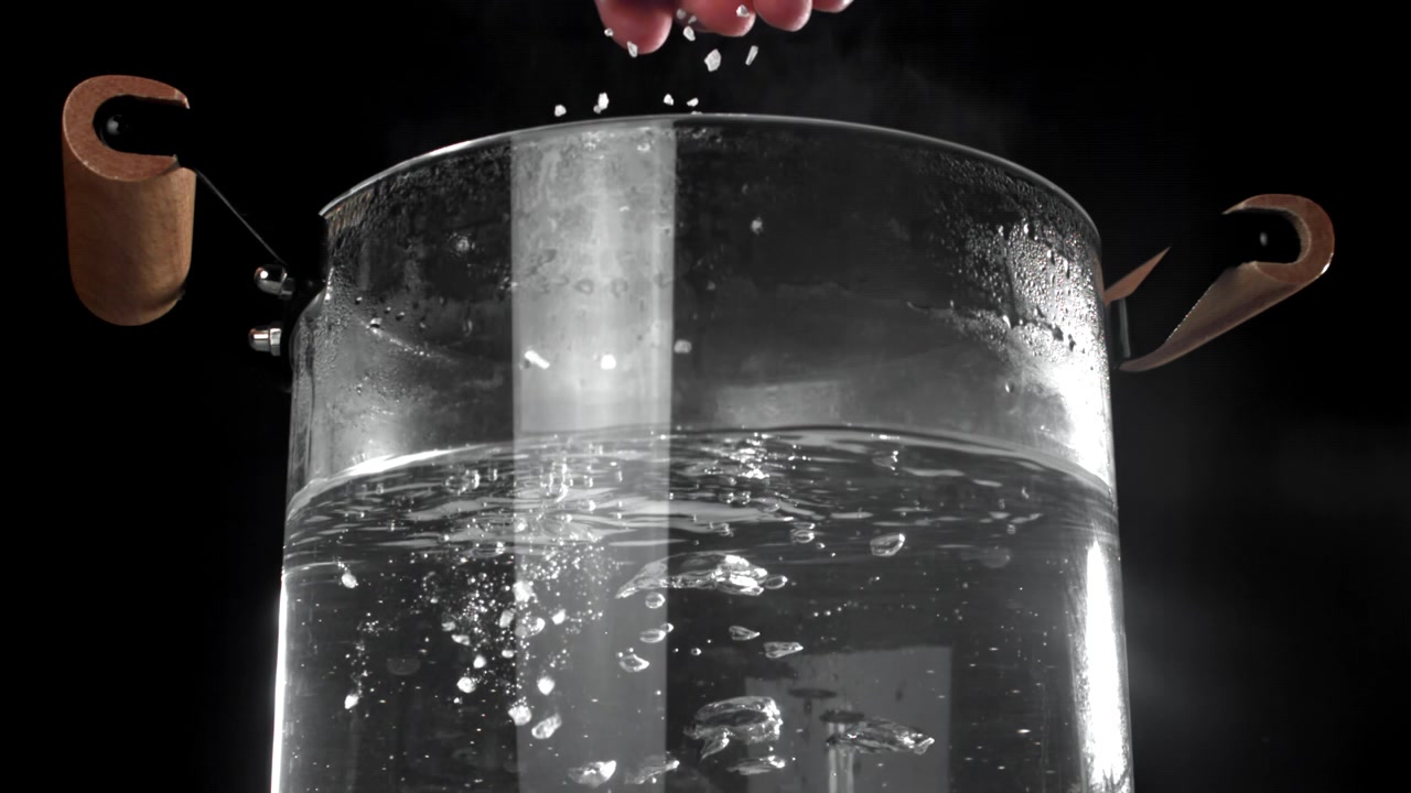 Mano che versa il sale nell'acqua bollente in una pentola di vetro