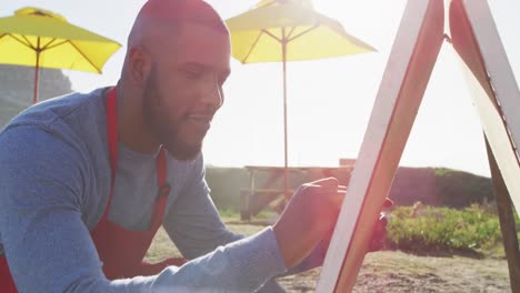 African-american-man-wearing-apron-writing-on-food-menu-slate-board-of-the-food-truck