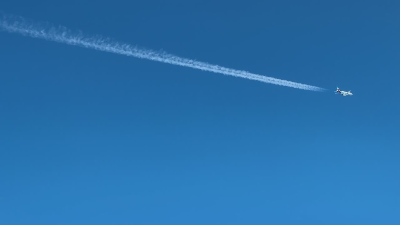 A cockpit view of a twin-engine jet airplane and its contrail crossing diagonally a blue sky. Aerial footage taken from another jet flying bellow with converging track. 4K