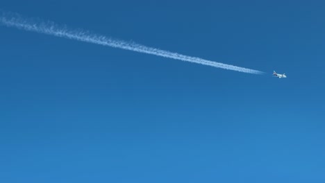 a cockpit view of a twin-engine jet airplane and its contrail crossing diagonally a blue sky. aerial footage taken from another jet flying bellow with converging track. 4k
