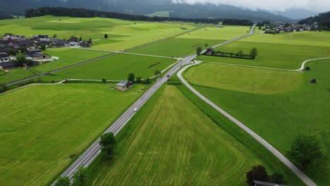 Alpine-Serenity:-4K-Aerial-Drone-Shot-of-Foggy-Drive-from-Graz-to-Hallstatt,-Cars-Wind-Through-Austrian-Countryside-with-perfectly-mowed-green-fields-and-Breathtaking-Alps-Panorama