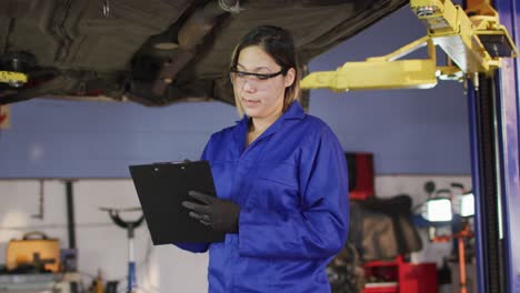 Porträt-Einer-Mechanikerin,-Die-Sich-Notizen-In-Der-Zwischenablage-Macht-Und-An-Einer-Autowerkstatt-Lächelt