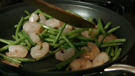 chef stirring king prawns and fine beans in pan for pad thai