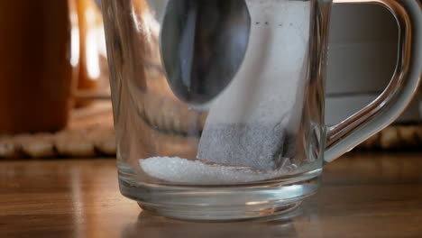 pouring sugar inside a transparent tea cup with a tea bag inside